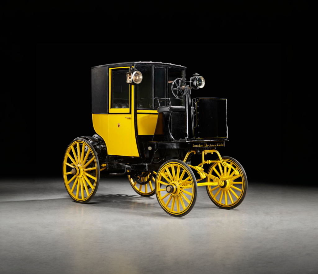 1897 Bersey electric taxi cab in black and yellow, displayed against a dark background.